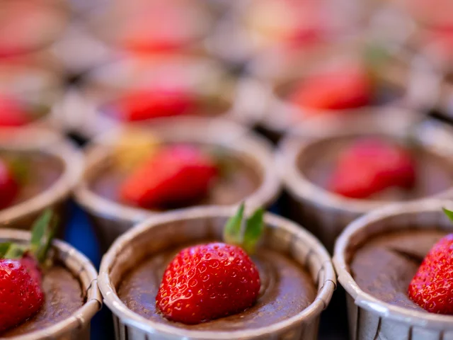 Une série de petits desserts au chocolat, joliment présentés dans des coupelles en papier, chacun garni d'une fraise fraîche. L'image est prise avec une faible profondeur de champ, mettant en valeur le dessert au premier plan.