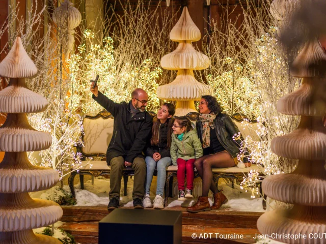 Famille prenant un selfie dans un décor lumineux de Noël au Château de Chenonceau.