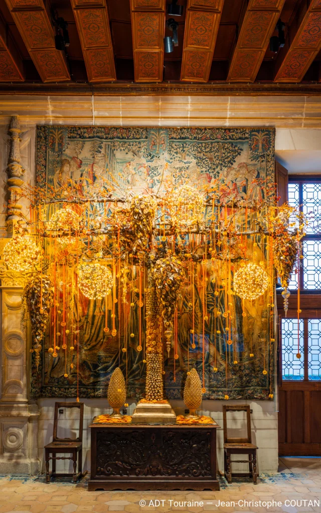 Décoration de Noël dorée et lumineuse devant une grande tapisserie au Château de Chenonceau.