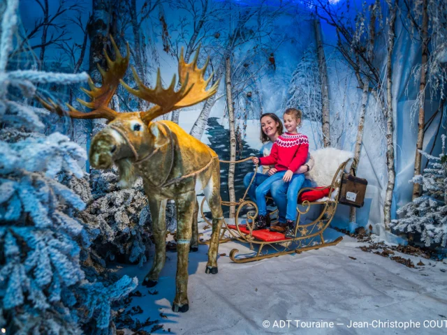 Une mère et sa fille installées dans un traîneau décoratif au château de Villandry, dans un décor de forêt enneigée.