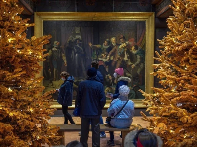 Visiteurs observant un grand tableau historique entouré de sapins dorés illuminés dans une salle décorée pour Noël au château de Blois.