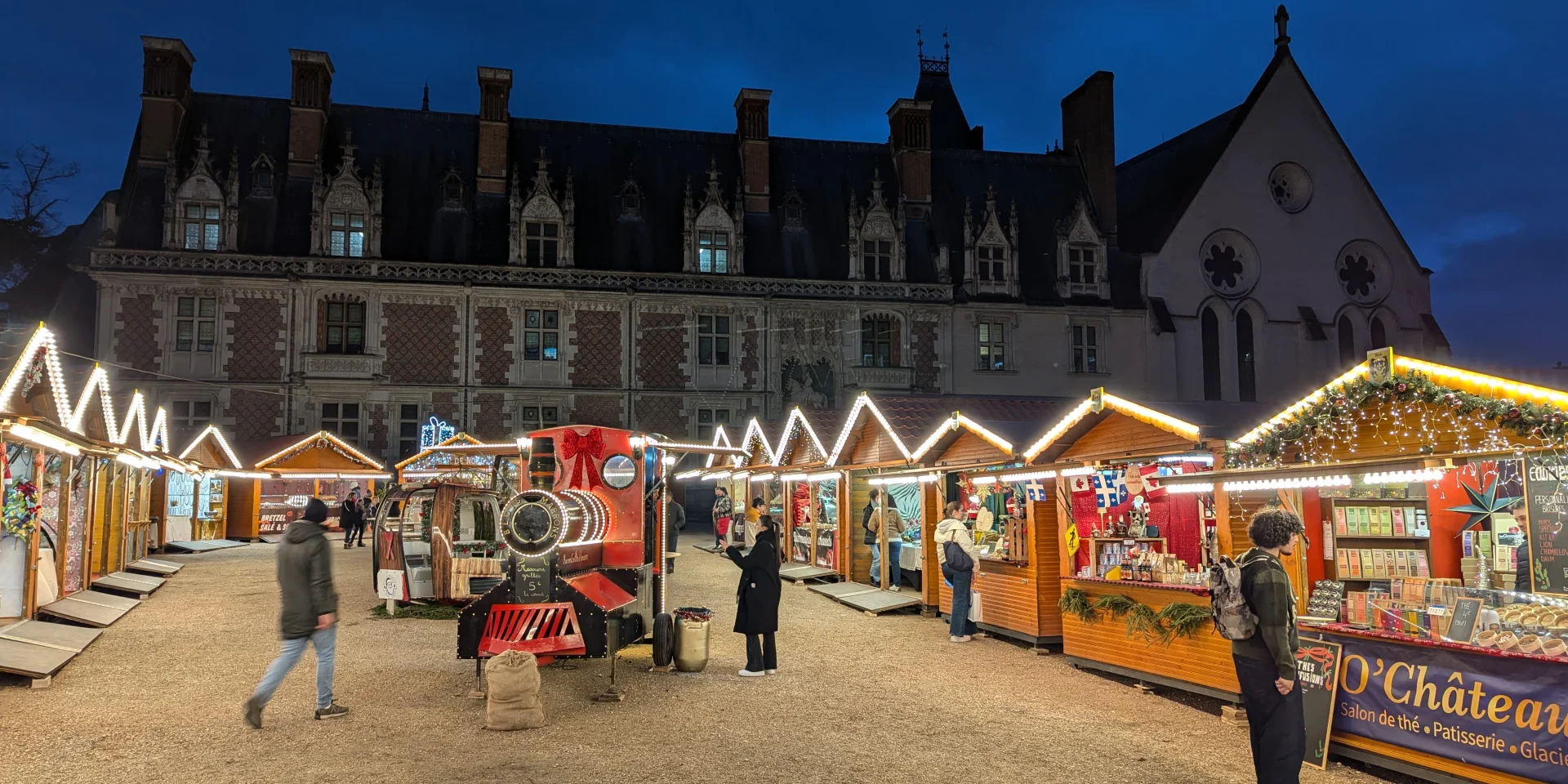 Marché de Noël illuminé devant le Château Royal de Blois, avec chalets en bois et décorations festives à la tombée de la nuit.