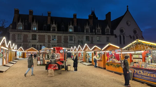 Marché de Noël illuminé devant le Château Royal de Blois, avec chalets en bois et décorations festives à la tombée de la nuit.