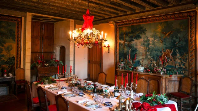 Salle à manger du château de Montpoupon décorée pour Noël avec chandelles rouges, vaisselle raffinée et tapisseries anciennes.
