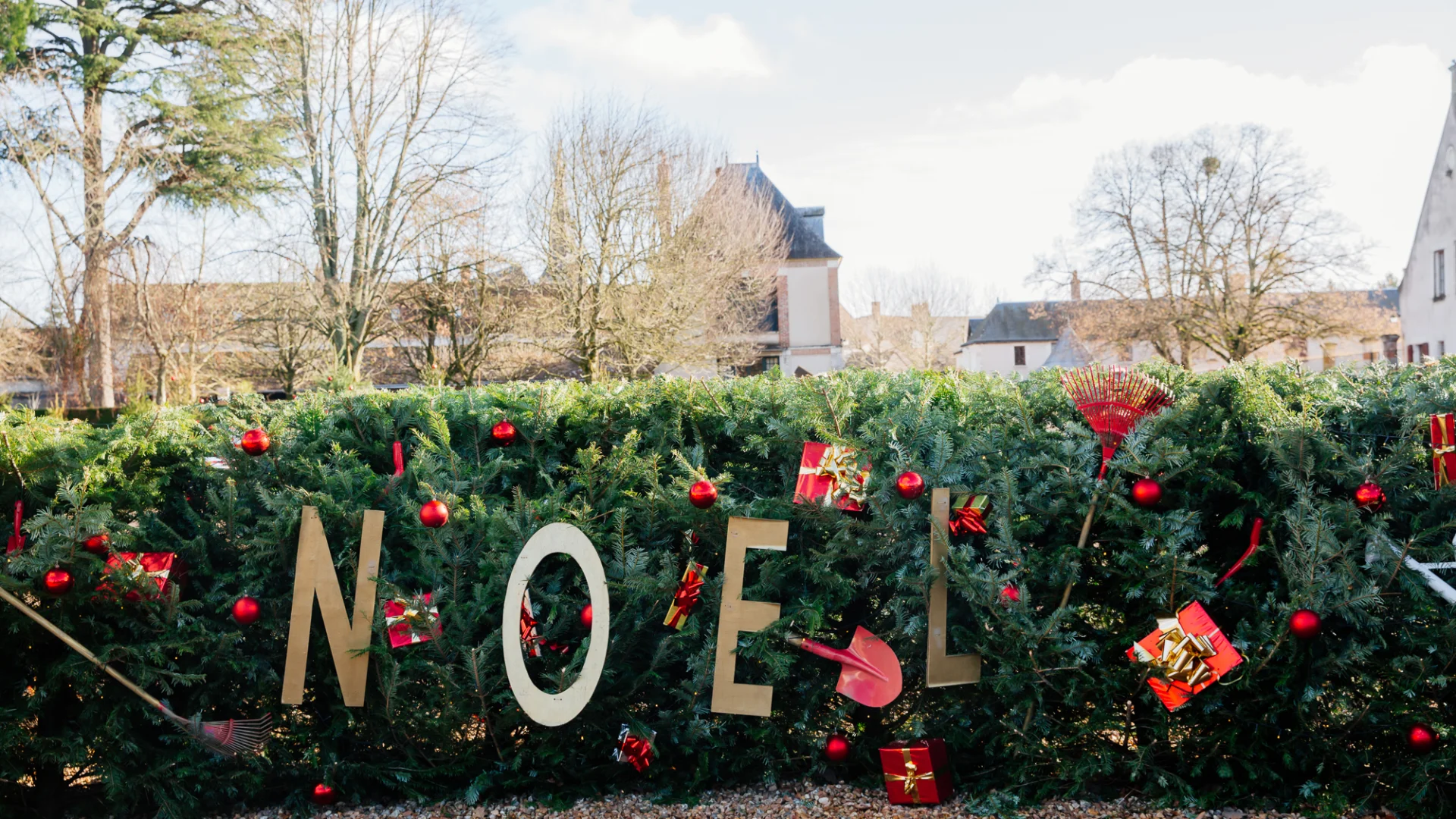 Décoration extérieure de Noël au château de Cheverny, avec les lettres dorées “NOËL” intégrées dans une grande haie de sapins ornée de boules rouges et de petits cadeaux.