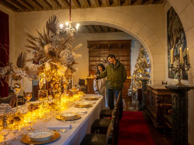 Salle du Château de Chaumont-sur-Loire décorée pour Noël, avec une grande table mise en scène de guirlandes lumineuses dorées et d’un centre de table végétal spectaculaire.