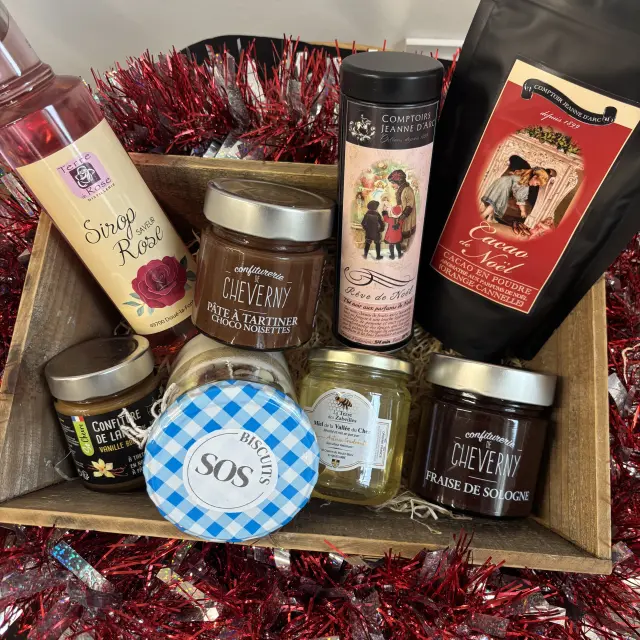 Panier gourmand composé de produits sucrés artisanaux du Val de Loire, dont confitures, pâte à tartiner, biscuits, miel et boissons, présenté dans une caisse en bois décorée de guirlandes rouges.