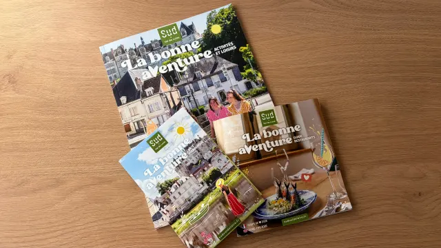 Trois brochures touristiques « Sud Val de Loire » posées sur une table en bois : un guide des activités et loisirs, une carte touristique et un guide des restaurants, tous sont intitulés « La bonne aventure ».