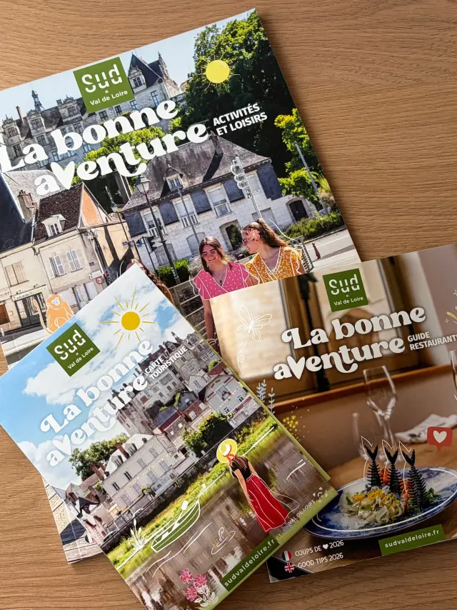 Trois brochures touristiques « Sud Val de Loire » posées sur une table en bois : un guide des activités et loisirs, une carte touristique et un guide des restaurants, tous sont intitulés « La bonne aventure ».