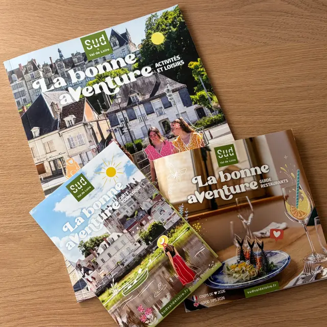 Trois brochures touristiques « Sud Val de Loire » posées sur une table en bois : un guide des activités et loisirs, une carte touristique et un guide des restaurants, tous sont intitulés « La bonne aventure ».
