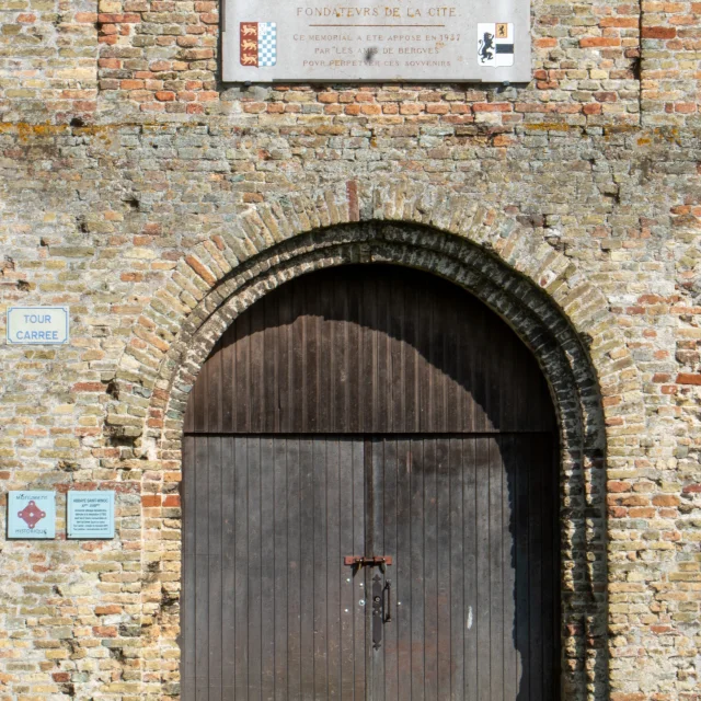Porte en bois de la Tour Carrée de l'Abbaye Saint Winoc Bergues avec des plaques explicatives sur les murs en briques jaunes