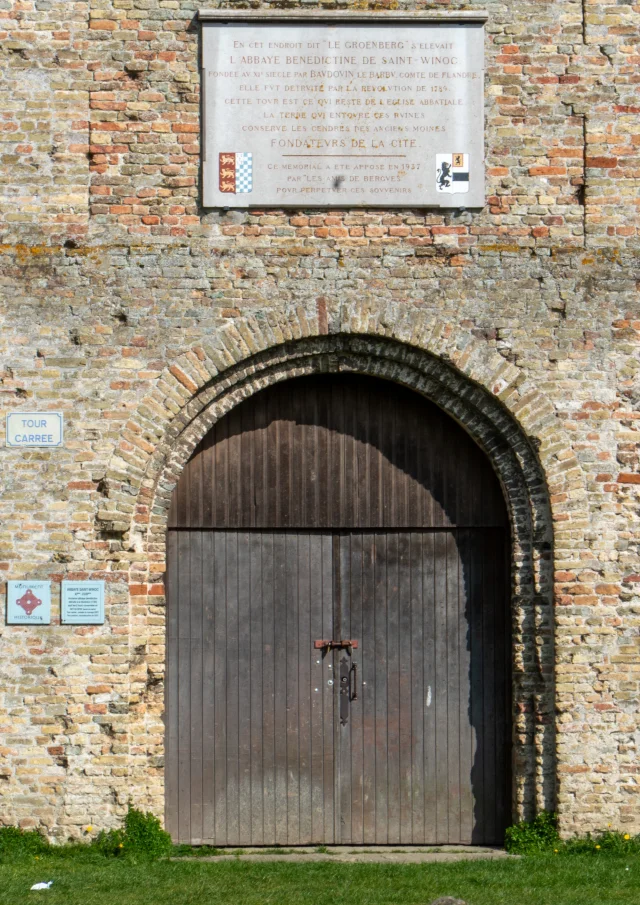 Wooden door of the Square Tower of the Abbey of Saint Winoc Bergues with explanatory plaques on the yellow brick walls