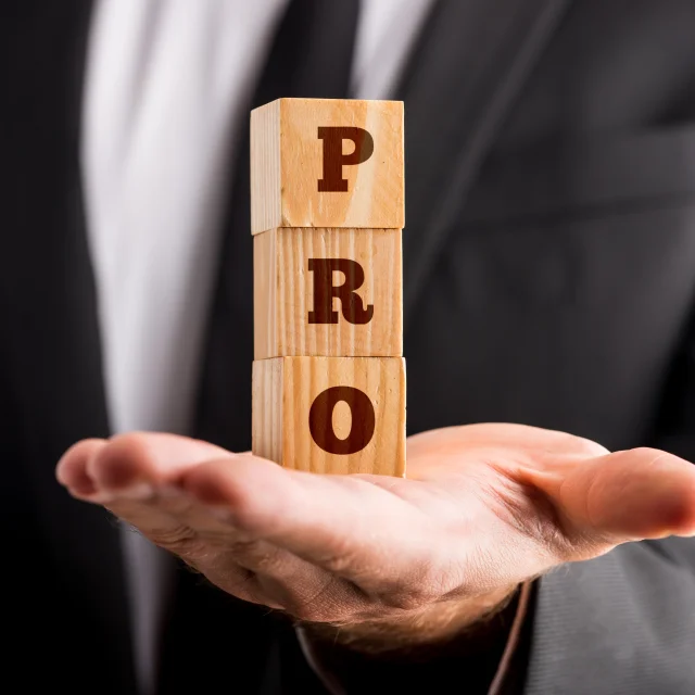 Zakenman houdt drie houten kubussen vast op de palm van zijn hand die een PRO-teken lezen. Conceptueel van professionaliteit en succes.