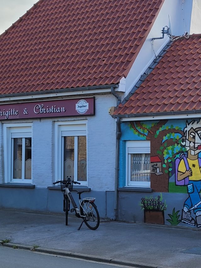 Vélo devant la façade et la fresque murale du café rando Au Tilleul à Bambecque