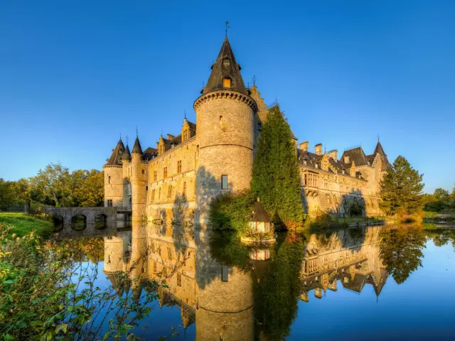 Stone castle with a central tower, surrounded by a lake and greenery