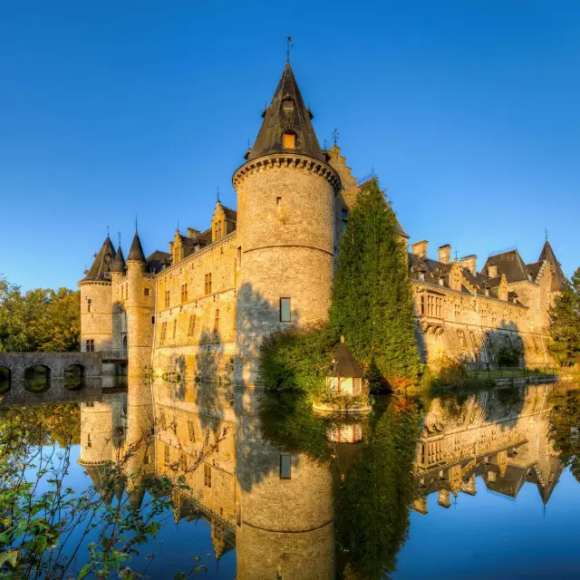 Stone castle with a central tower, surrounded by a lake and greenery