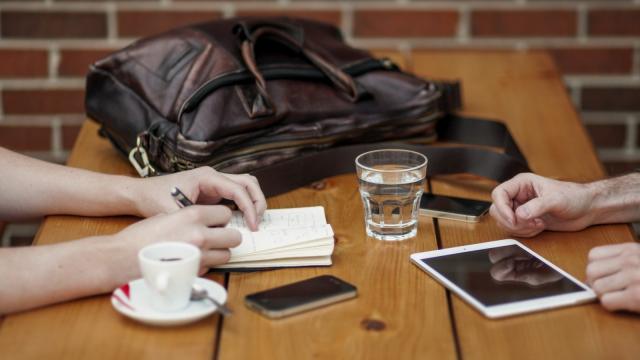 Friends Sitting In Cafe Writing In Notebook With Digital Tablet And Coffee Cup