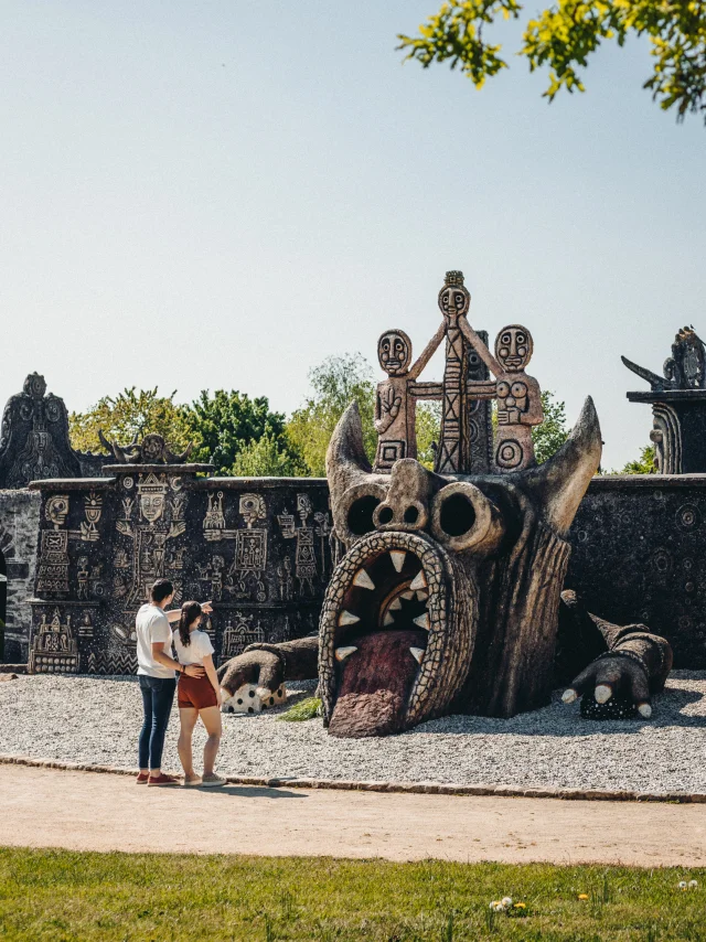 Plan large de l'archi-sculpture de Robert Tatin. Un couple de dos observe une des composante de cette immense sculpture : le dragon