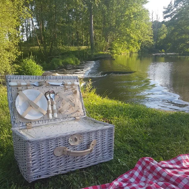 Une nappe vichy et un panier pique nique sont installés au bord de la rivière