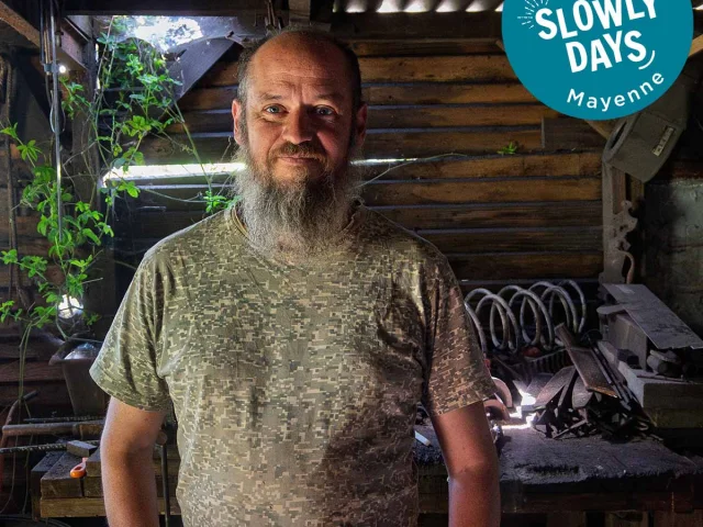 Emmanuel Davoust, coutelier-forgeron à Vaiges, dans son atelier traditionnel entouré de ses outils. En haut à droite de l'image on peut voir l'estampille Slowlydays en blanc sur fond bleu
