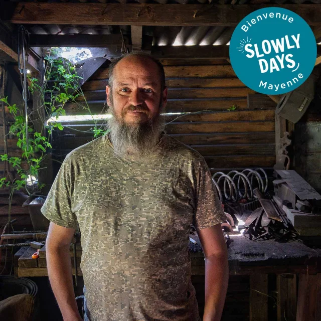 Emmanuel Davoust, coutelier-forgeron à Vaiges, dans son atelier traditionnel entouré de ses outils. En haut à droite de l'image on peut voir l'estampille Slowlydays en blanc sur fond bleu