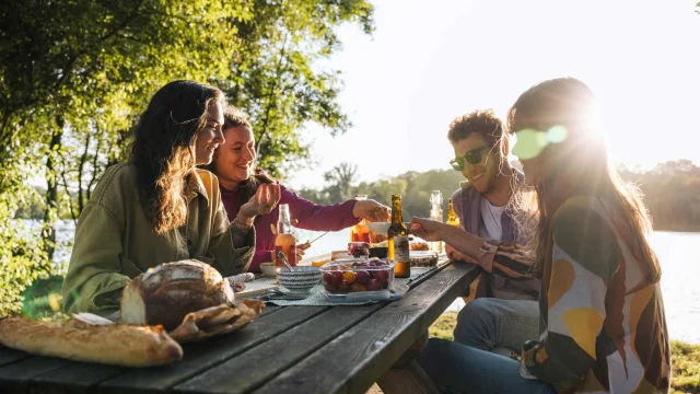 Groupe d’amis en pique-nique au bord d’un étang, partageant un repas au coucher du soleil.