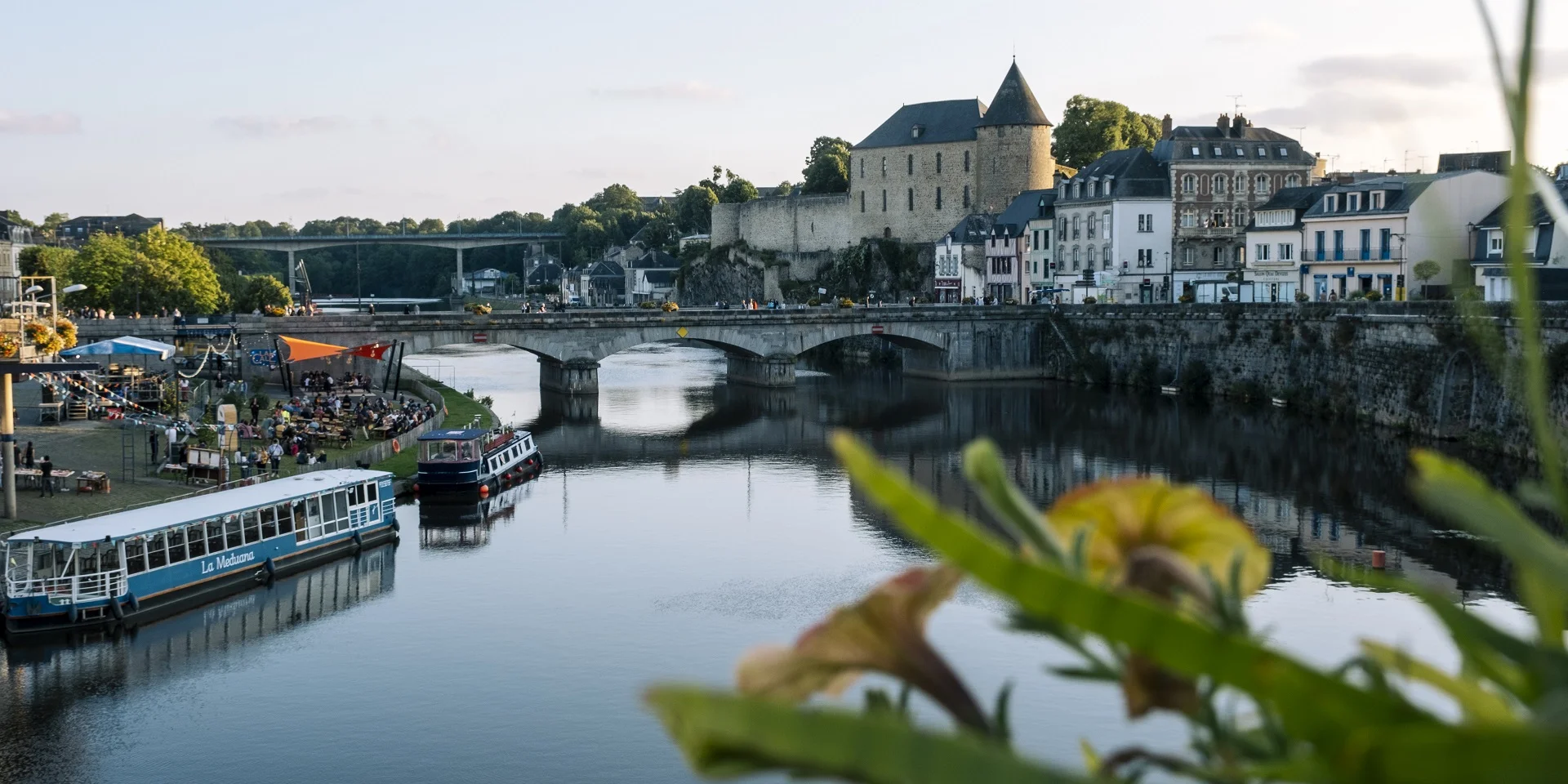 La ville de Mayenne, douce lumière de fin de journée. Vue sur le château, la rivière et le bateau La Meduana.