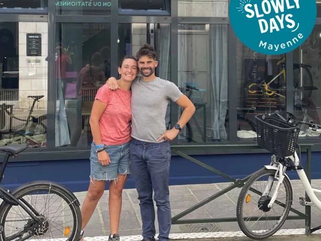 Marine et Damien posent souriants devant leur établissement Tartine & Rustine à Laval. Ils sont , entourés de vélos. Un badge Bienvenue SlowlyDays Mayenne apparaît en haut à droite de l'image.