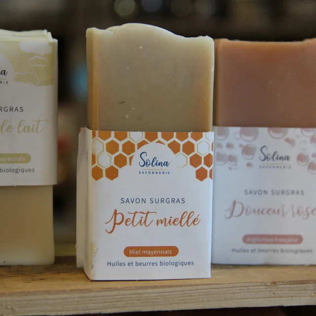 Trois savons surgras artisanaux Solina aux parfums de lait de vache mayennais, miel mayennais et argile rose française, posés sur une étagère en bois.