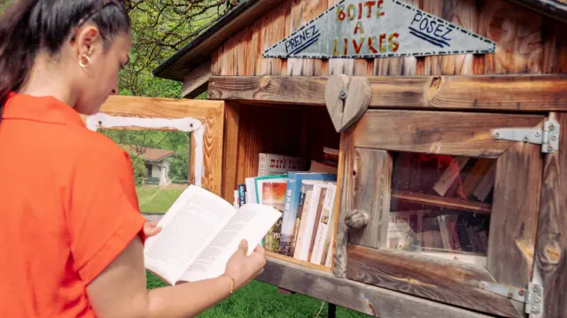 Une randonneuse lit un livre dans une boite à livre en bois