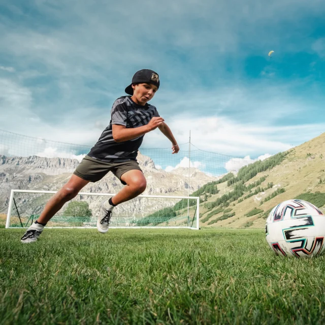 Enfant qui joue au foot, été, terrain de foot, vue montagne