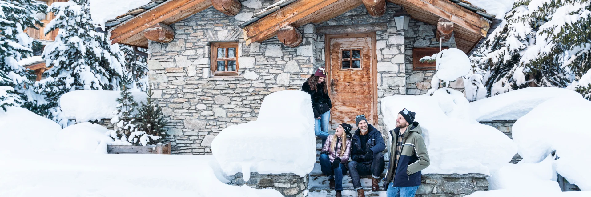 A group of friends laughing in front of a snow-covered chalet in Val d'Isère.