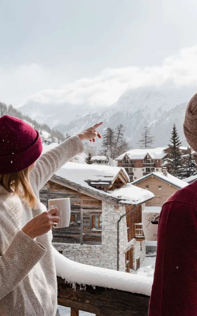 Deux personnes (amis ou couple) sur un balcon enneigé d'un chalet à Val d'Isère en hiver