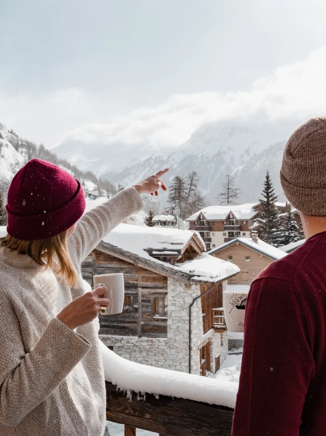 Deux personnes (amis ou couple) sur un balcon enneigé d'un chalet à Val d'Isère en hiver