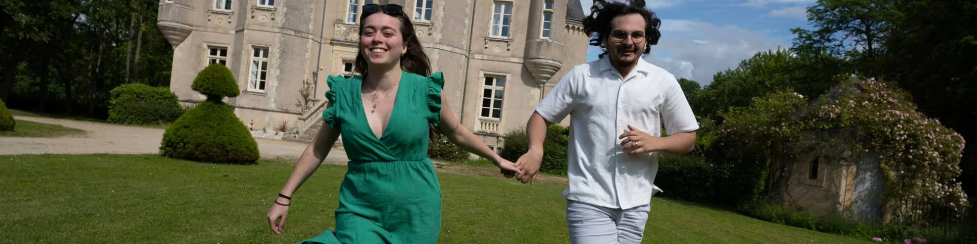 un couple qui se tiennent main dans la main et qui court avec le château de la grange moreau derrière eux