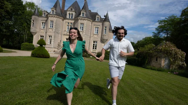 un couple qui se tiennent main dans la main et qui court avec le château de la grange moreau derrière eux