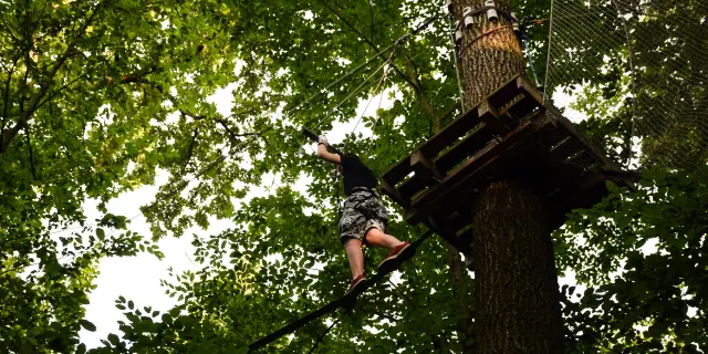 Young guy runs an obstacle course from tree to tree on a rope park