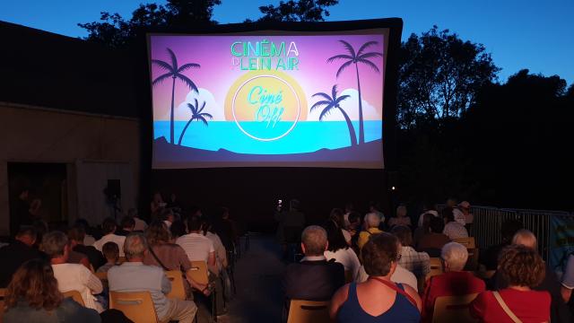 Cinéma en plein air avec écran et public.