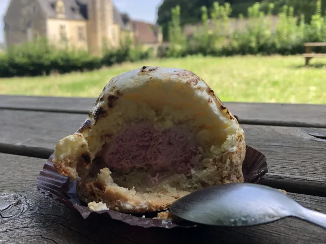 Gâteau individuel blanc avec coeur rose sur une table de pique-nique avec en fond de la verdure et un manoir