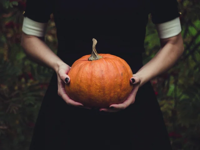 Femme (où on ne voit que les mains et le buste) tenant dans sa main une citrouille