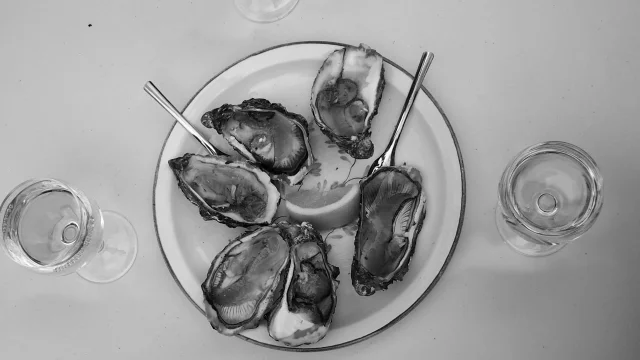 Photo en noire et blanc : vue plongée sur une table ronde blanche avec huitres au milieu et 4 verres de vin blanc autour