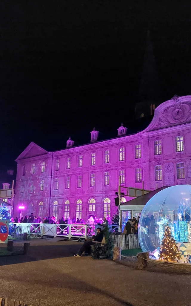 Grand bâtiment de nuit avec devant patinoire, boule de Noël XXL avec une lumière rose