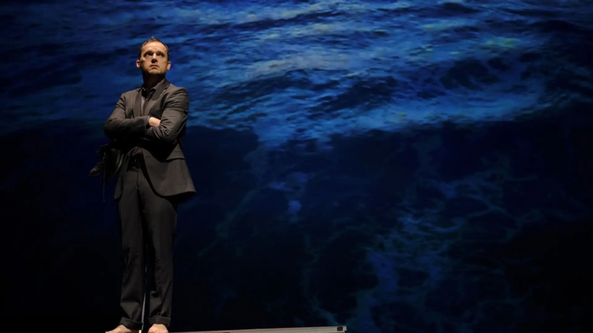 Homme surélevé en costume devant toile bleue les bras croisés