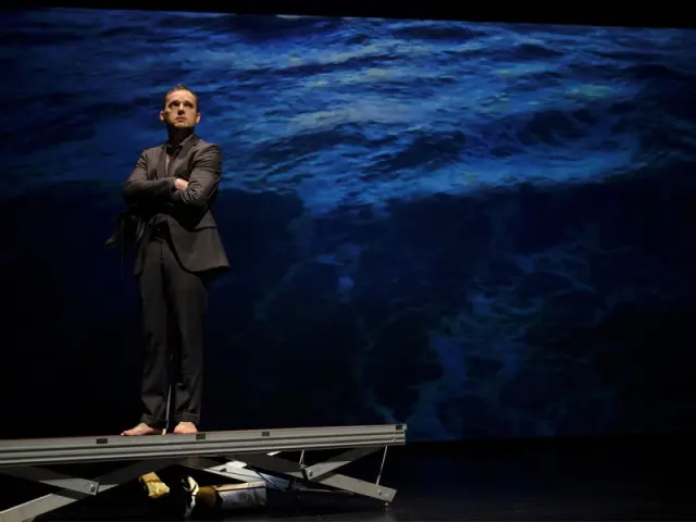 Homme surélevé en costume devant toile bleue les bras croisés
