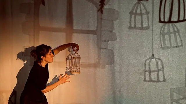 Femme avec une toile en fond et une cage à oiseau dans la main