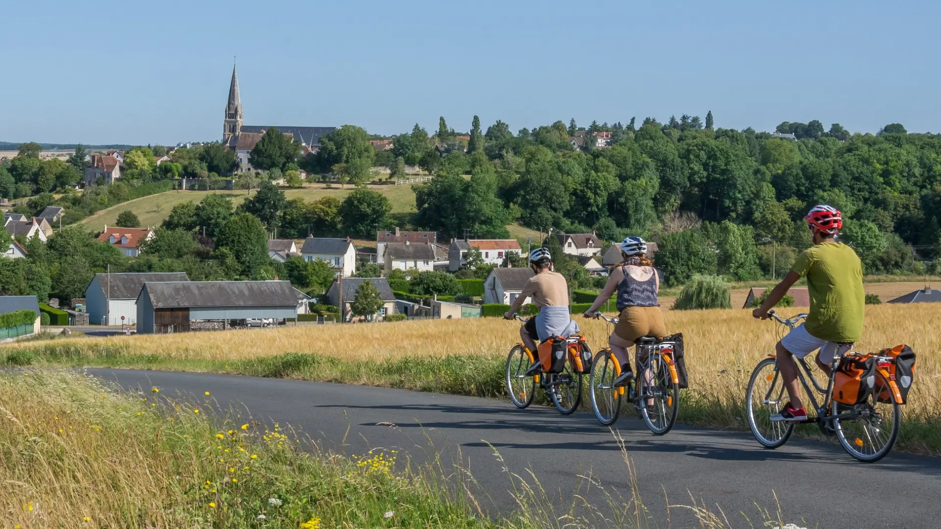 3 cyclos sur la route avec champs sur les cotés et village en fond