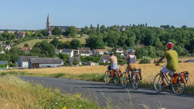 3 cyclos sur la route avec champs sur les cotés et village en fond