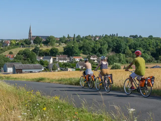 3 cyclos sur la route avec champs sur les cotés et village en fond