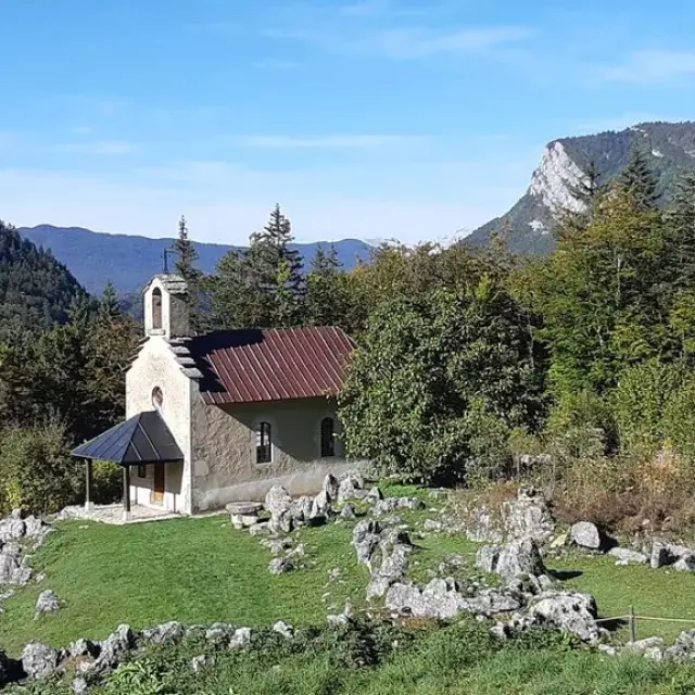 Petite chapelle en pierre avec un toit rouge, entourée de rochers et de verdure