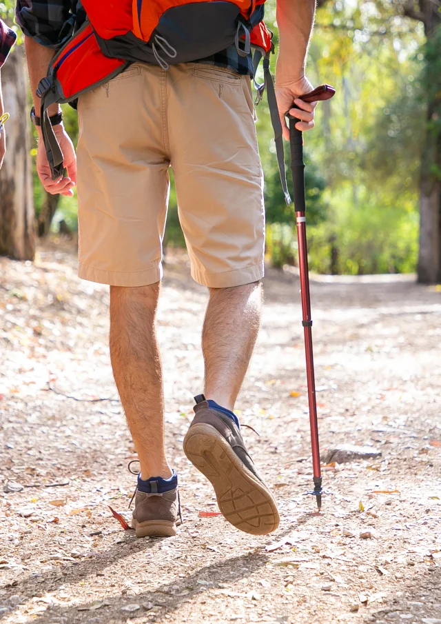 Back view of couple hiking together on road. Unrecognizable man and woman walking on nature. Legs of tourists trekking with backpacks in sunny day. Tourism, adventure and summer vacation concept
